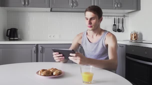 Genç adam evde mutfakta otururken video oyunu oynamak için dijital tablet kullanıyor — Stok video