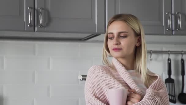 Nettes Mädchen in einer karierten Decke trinkt Tee und schaut morgens aus dem Fenster in der Küche — Stockvideo