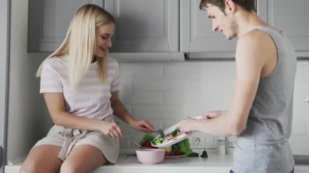 Ung kille och flicka sitter på bordet skär grönsaker tillsammans för sallad till lunch i köket — Stockvideo