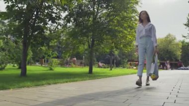 Güzel genç bir kadın elinde sebzelerle pamuk örgüsü alışveriş torbası tutuyor ve yaz parkında yürüyor.