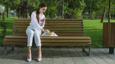 Genç kadın, yaz parkında meyve ve sebzelerle dolu pamuk örgülü alışveriş çantasıyla bankta oturuyor. Sıfır atık.