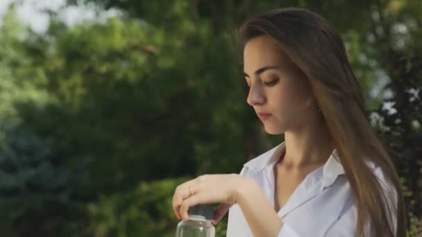 Jovem mulher bonita bebendo suco de laranja ao ar livre no parque de verão — Vídeo de Stock