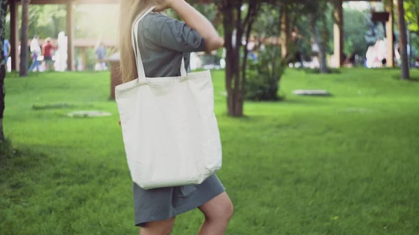 Side view of Young girl holds white textile eco bag and walks in the summer park — Stock Photo, Image