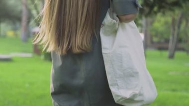 Genç kız beyaz tekstil çantasını tutuyor ve yaz parkında yürüyor.