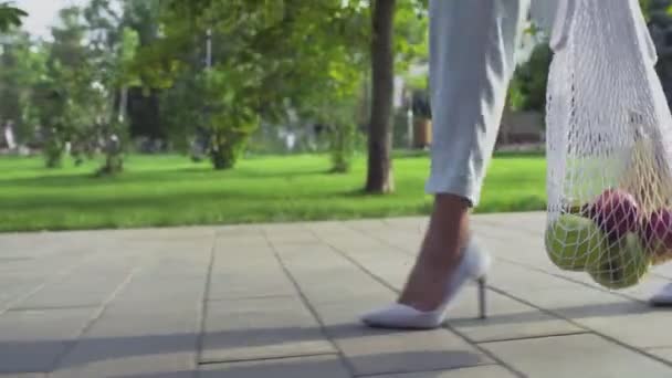 Közelkép a nő tartja pamut háló bevásárló táska gyümölcsökkel és séták a nyári parkban — Stock videók