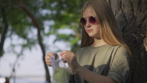 夏の公園の木の近くにサングラスをかけている若い女性は、綿メッシュのショッピングバッグからリンゴを取ります。廃棄物ゼロショッピング. — ストック動画