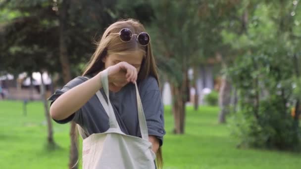 Jovem em óculos de sol bebendo suco de laranja ao ar livre no parque de verão — Vídeo de Stock