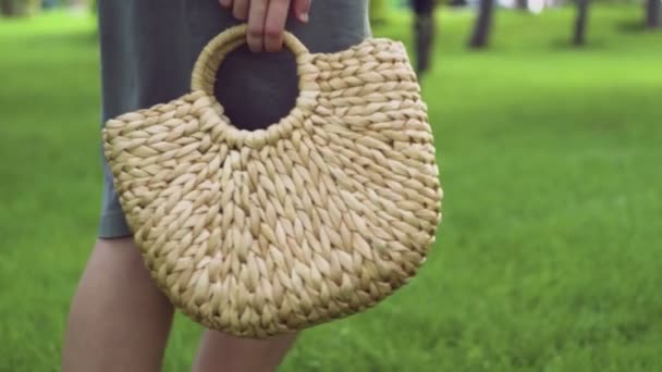 Mujer joven con bolso de paja elegante hecho a mano camina en el parque de verano. Bolsa ecológica . — Vídeos de Stock