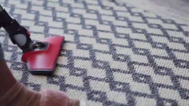 Halıyı temizlemek için elektrikli süpürge kullanan genç bir kadın.
