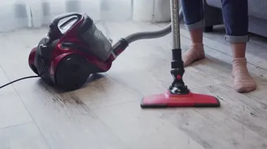 Yerde elektrikli süpürge kullanan genç bir kadın.