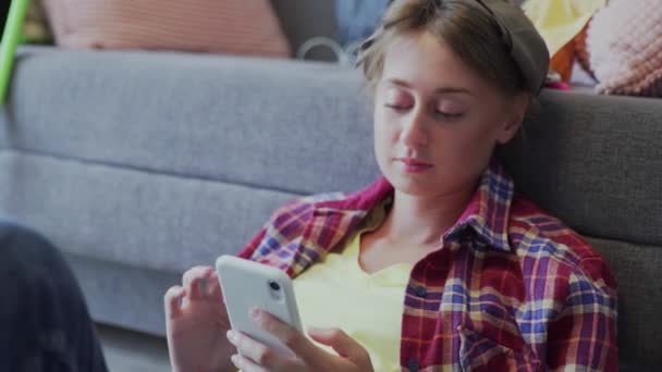 Mooie jonge vrouw rust op de vloer na het schoonmaken en het gebruik van de telefoon — Stockvideo