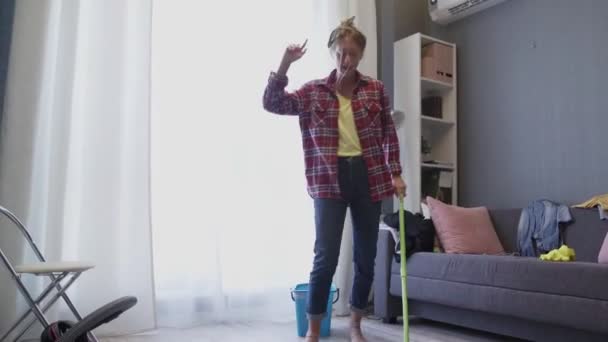 Счастливая молодая женщина симпатичная домохозяйка моет пол шваброй и танцует дома — стоковое видео
