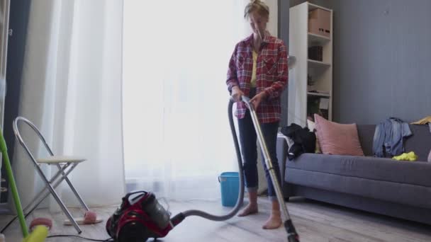 Γυναίκα χρησιμοποιούν ηλεκτρική σκούπα για τον καθαρισμό του δαπέδου στο σαλόνι κατά τη διάρκεια της καθημερινής καθαρισμού. — Αρχείο Βίντεο