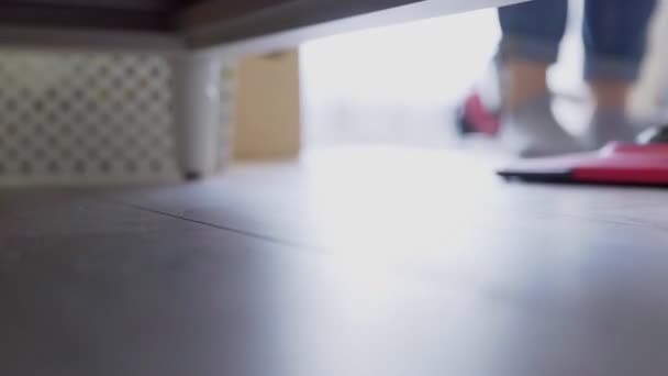 女性はベッドの下の床を掃除するために掃除機を使う — ストック動画