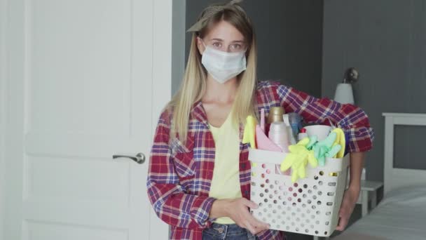 Woman with mask on face and Basket full of sponges and household chemicals look at camera — Stock Video