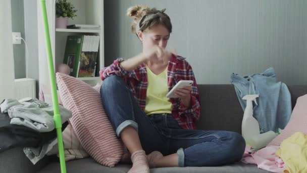 Beautiful young woman is resting on the sofa after cleaning and using the phone — Stock Video