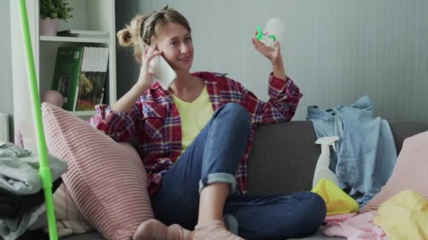 Красива молода жінка відпочиває на дивані після прибирання і розмови по телефону — стокове відео