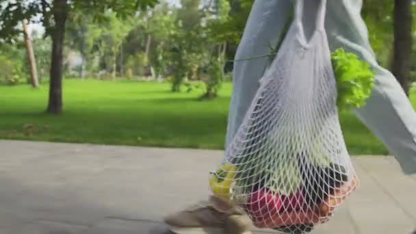 Mulher irreconhecível detém saco de compras de malha de algodão com legumes e passeios no parque de verão — Vídeo de Stock