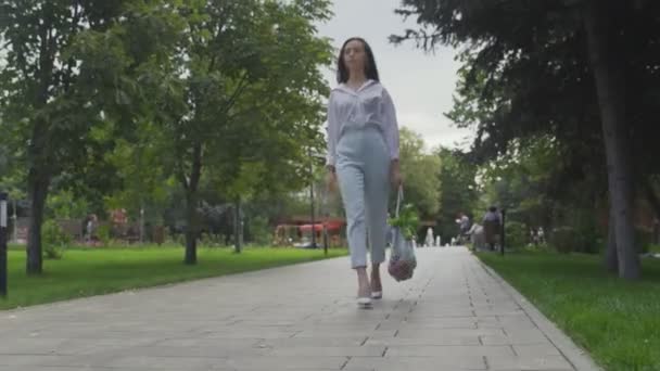 Ung kvinna håller bomull mesh shoppingväska med grönsaker och promenader i sommarparken. Handeln med nollavfall. — Stockvideo