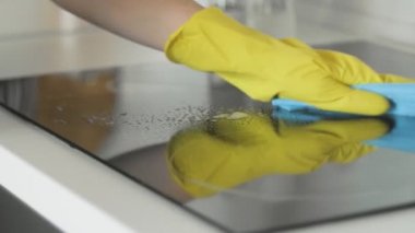 Mutfakta, sarı lastik eldivenli bir kadın tarafından yağlı temizleme spreyi ve mavi paçavrayla yemek pişirme paneli..