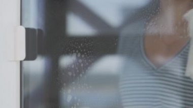 Sarı eldivenli genç bir kadın camları beyaz bez ve deterjanla yıkıyor..