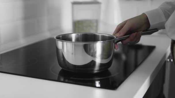 El primer plano de la mujer pone una olla y enciende la cocina de inducción — Vídeos de Stock