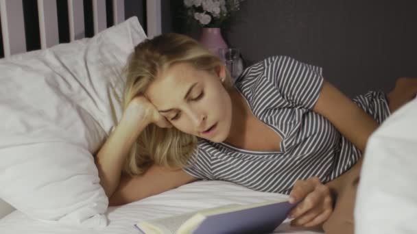 Fiatal lány fekszik az ágyon, és könyvet olvas szabadidejében. — Stock videók