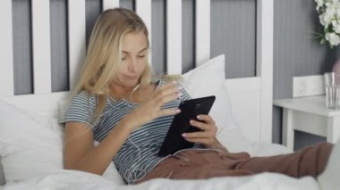 Genç, sıkılmış bir kadın sosyal medyada geziniyor. Tabletle evde bir yatakta yatıyor.