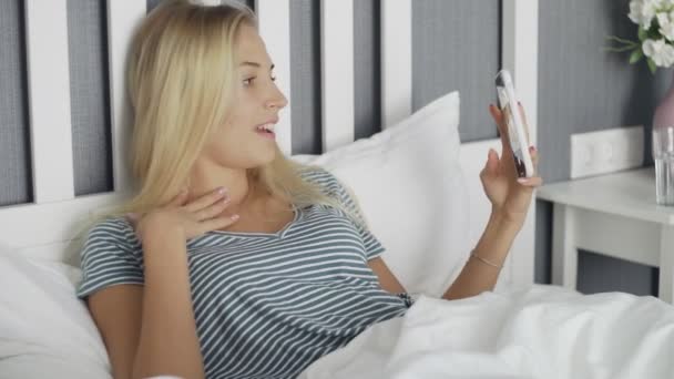 Sonriente feliz hermosa joven acostada en la cama en el dormitorio cómodo y tomando video selfie — Vídeos de Stock