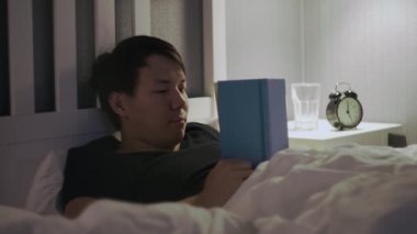 Genç adam yatakta uzanıp kitap okuyor ve sonra uykuya dalıyor.