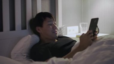 Tablet bilgisayarlı genç Asyalı adam yatakta yatıyor.