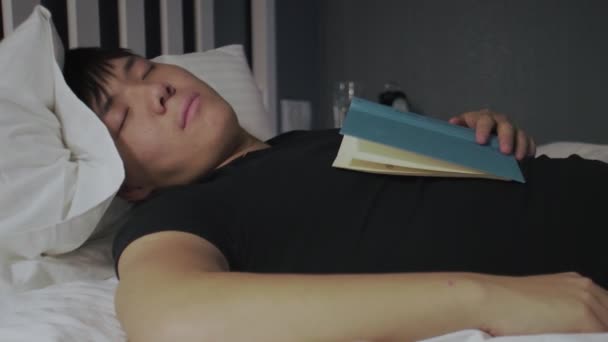 Mladý asijský muž spí s knihou na hrudi — Stock video