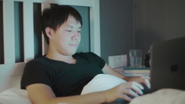 Jung asiatisch mann using ein laptop spät bei nacht im bett — Stockvideo