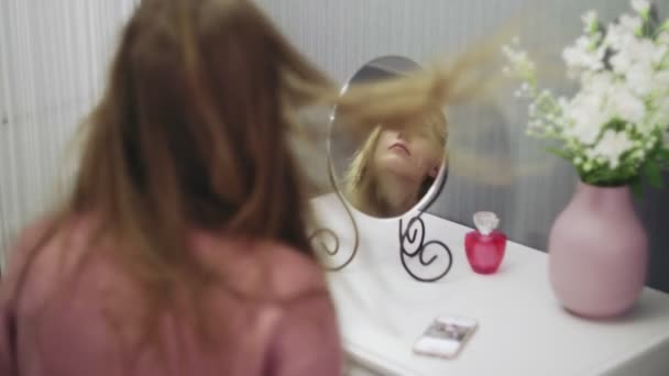 Gyönyörű fiatal nő használ hajszárítót, miközben belenéz a tükörbe a szobában. — Stock videók