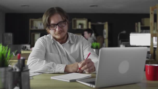 Joven gerente está trabajando en la escritura de oficina sentado en el escritorio solo — Vídeo de stock