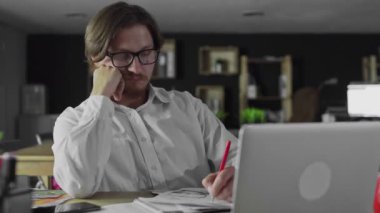 Genç müdür, büroda oturan belgeleri izliyor.
