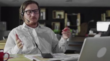 Kulaklıklı genç müdür ofiste dizüstü bilgisayarla çalışıyor.