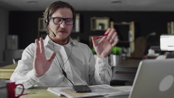 Менеджер в наушниках работает на ноутбуке в офисе — стоковое видео