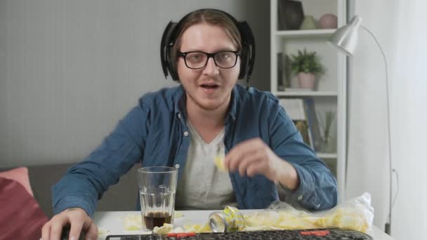 Joven concentrado jugando videojuegos, comiendo papas fritas y bebiendo cola — Vídeos de Stock