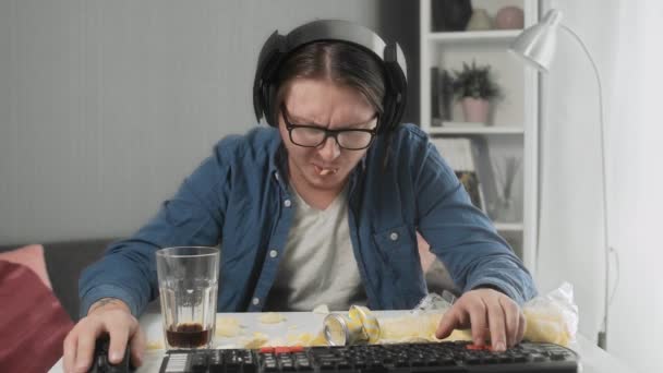 Skoncentrowany młody człowiek gra w gry wideo i dławi się chipsami — Wideo stockowe