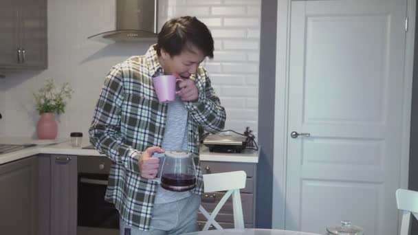 Junge asiatische Mann gähnen und trinken Kaffee in Küche zu Hause — Stockvideo