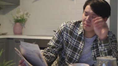 Uykulu Asyalı adam kahve içiyor ve masada gazete okuyor..