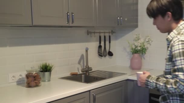 Asiático hombre tomando una galleta y beber café en casa en la cocina . — Vídeo de stock