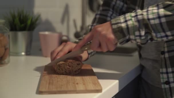 도마 위에 얇게 썬 갈색 빵의 근접 사진. 사람 은씨로 검은 빵을 베어 낸다 — 비디오