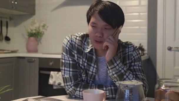 집 부엌에서 휴대 전화로 통화하는 아시아 남자 — 비디오