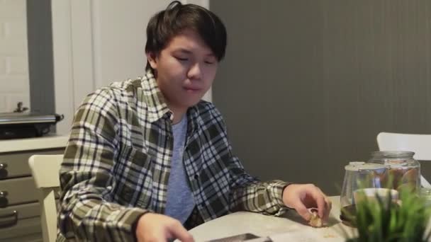 Uykulu Asyalı adam kurabiye yiyor ve masada gazete okuyor.. — Stok video
