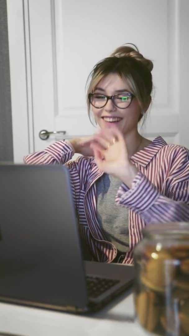 会議の呼び出しによって通信する若い幸せな女性の垂直ビデオは台所でコンピュータを見て話す. — ストック動画