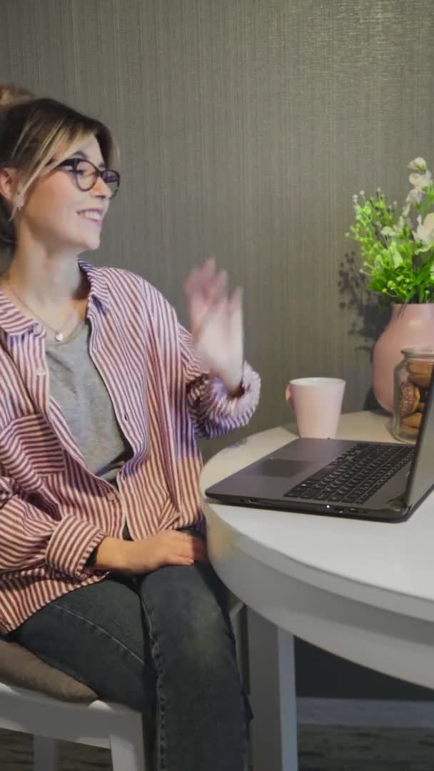 วิดีโอแนวตั้งของหญิงสาวสื่อสารโดยการประชุมทางโทรศัพท์พูดคุยมองไปที่คอมพิวเตอร์และดื่มกาแฟที่ห้องครัว . — วีดีโอสต็อก