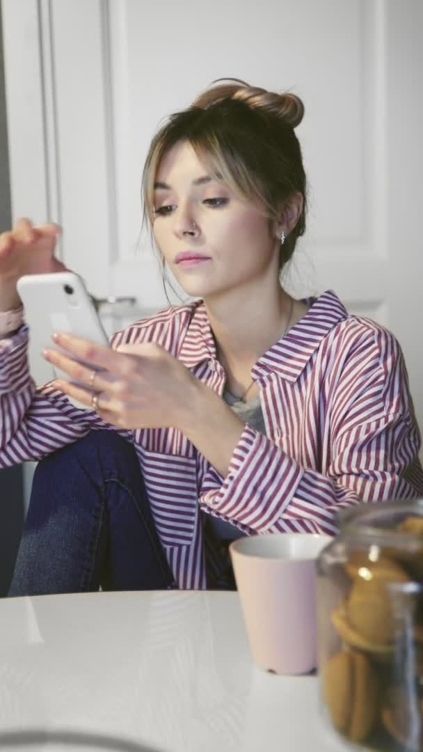 Vídeo vertical de la joven atractiva mujer caucásica tocando, desplazándose y escribiendo en el teléfono inteligente — Vídeo de stock