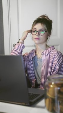 Mutfakta dizüstü bilgisayarla çalışan genç bir kadının dikey videosu..